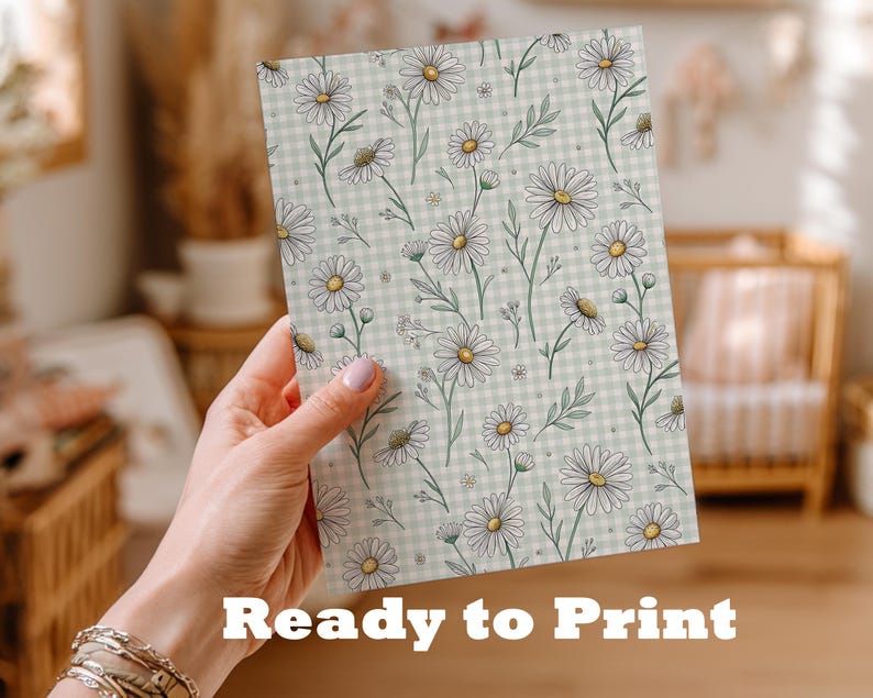 A hand holding a card with a floral pattern on it, in a room with a crib and other furniture.