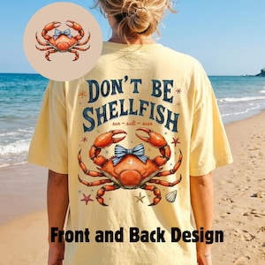 May include: A light yellow t-shirt with a crab graphic and the text "DON'T BE SHELLFISH". The crab has a blue bow tie. The shirt also has a crab graphic on the front. The words "sun - salt - sass" are also on the shirt.