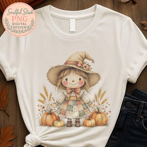 May include: White t-shirt featuring a watercolor illustration of a scarecrow doll wearing a hat and patchwork dress, surrounded by pumpkins and wheat. The shirt has the text "Soulful Stash PNG Digital Design" in a circular logo.