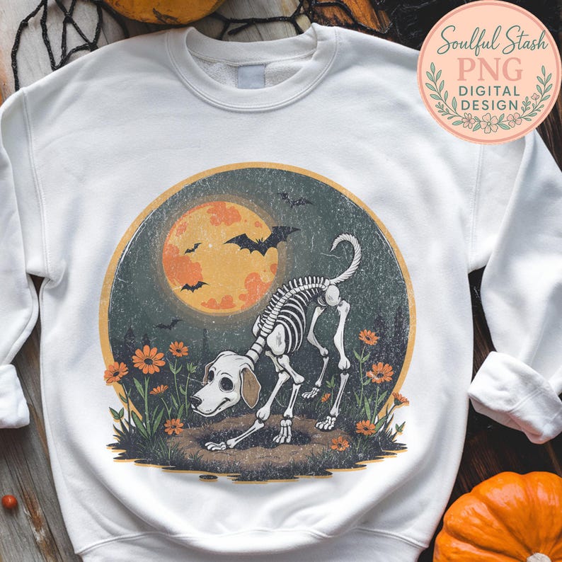 May include: White sweatshirt featuring a Halloween-themed graphic. The design includes a dog skeleton, an orange moon, bats, and flowers. The sweatshirt has a crew neck and long sleeves. The text "Soulful Stash PNG Digital Design" is also visible.