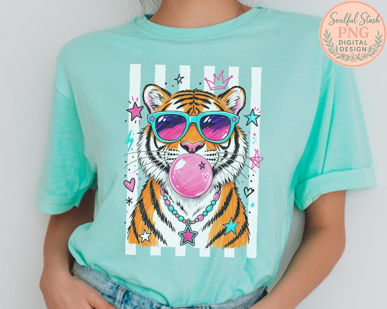A person wearing a turquoise t-shirt with a graphic design of a tiger blowing a bubble gum bubble, surrounded by colorful stars and hearts.