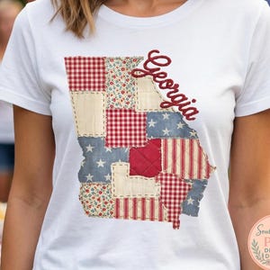 Puede incluir: Camiseta blanca con un diseño de patchwork del estado de Georgia. El diseño incorpora telas rojas, blancas y azules con estampados florales, de cuadros y de estrellas. La palabra "Georgia" está escrita en cursiva.