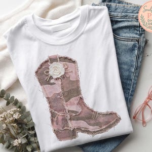 May include: White t-shirt featuring a pink and brown patchwork cowboy boot design with a white flower accent. The shirt is laid on a white surface with blue jeans and pink glasses. The text "Soulful Stash PNG Digital Design" is in the upper right corner.