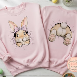Könnte beinhalten: Zwei hellrosa Sweatshirts. Eines zeigt ein Hasengesicht mit einer rosa Schleife, die aus einer zerbrochenen Oberfläche kommt. Das andere zeigt das Hinterteil und die Pfoten eines Hasen. Die Sweatshirts sind Teil eines digitalen Designs.