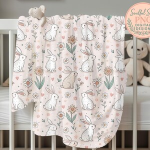 A white crib with a pink blanket featuring a repeating pattern of rabbits and flowers.