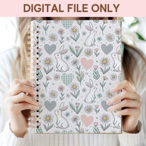 A person is holding a spiral-bound notebook with a floral and rabbit pattern printed on it.