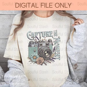 May include: A beige t-shirt with a vintage camera graphic and the text "Capture the Moment". The camera is surrounded by flowers and greenery.