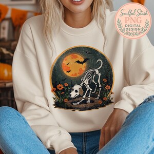 May include: Cream-colored sweatshirt featuring a Halloween-themed graphic. The design includes a skeleton dog in front of a full moon, bats, and flowers. The text "Soulful Stash PNG DIGITAL DESIGN" is in a circular logo on the upper right.