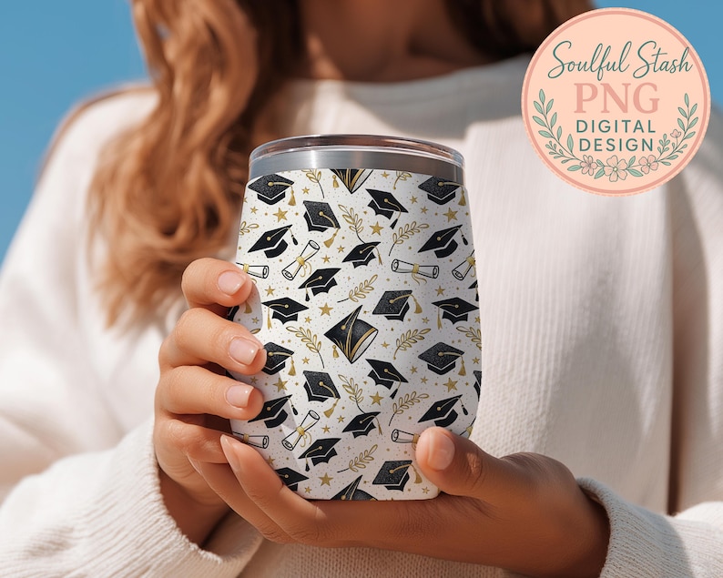 A person is holding a white wine glass with a pattern of black graduation caps and laurels on it.