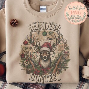 May include: Beige sweatshirt featuring a reindeer wearing a Santa hat, with the words "REINDEER HUNTER" in a vintage style. The design includes rifles, Christmas ornaments, and a target.