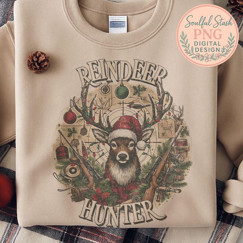 May include: Beige sweatshirt featuring a reindeer wearing a Santa hat, with the words "REINDEER HUNTER" in a vintage style. The design includes rifles, Christmas ornaments, and a target.