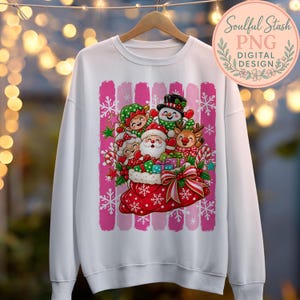 Op de afbeelding: Een wit sweatshirt met ronde hals en een grafische print van de Kerstman, Kerstvrouw, een elf, een sneeuwpop en een rendier die uit een rode cadeautas komen. Het ontwerp bevat roze verticale strepen, witte sneeuwvlokken en kleurrijke cadeaus.