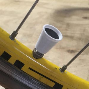 May include: A white valve stem cap with a black rubber insert. The cap is attached to a bicycle tire valve.