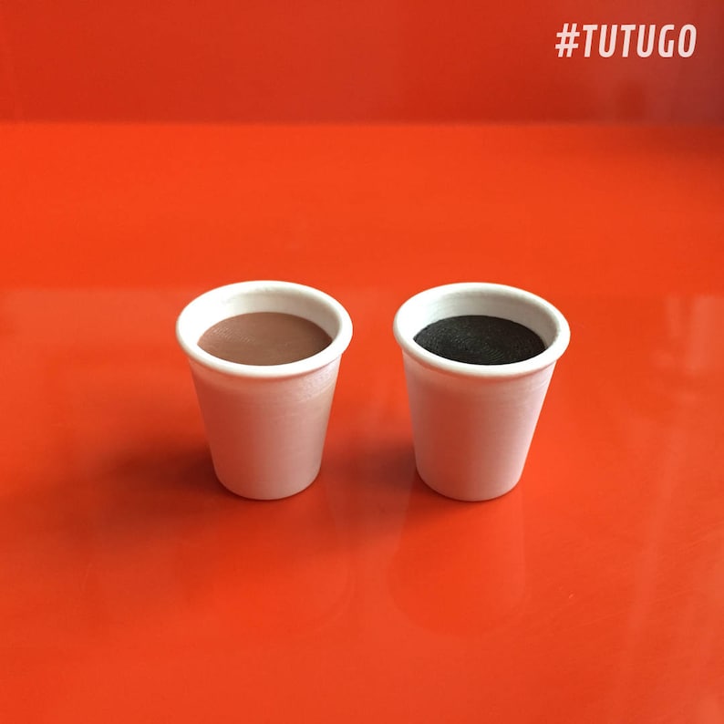 May include: Two white styrofoam cups, one filled with brown liquid and the other with black liquid, on a red surface. #TUTUGO