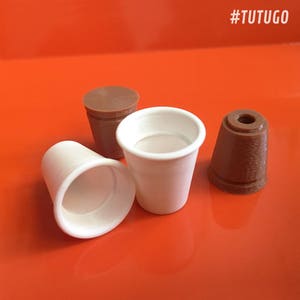May include: Three small cups, two white and one brown, on a bright orange surface. The white cups are made of paper and the brown cup is made of plastic.