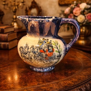 May include: Antique ceramic pitcher with a blue and white speckled rim and handle. The body of the pitcher features a detailed illustration of a horse-drawn carriage in shades of red, black, and cream. A classic decorative piece.