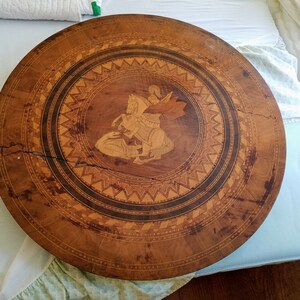 May include: Round wooden table top with intricate inlaid design. The center features a detailed image of a knight on horseback. The border has geometric patterns and dark brown accents. The table top is approximately 36 inches in diameter.