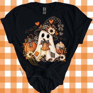 Op de afbeelding: Een zwart t-shirt met een afbeelding van een witte geest die een zwarte heksenhoed met een zonnebloem draagt en een kleine oranje pompoen vasthoudt. Het ontwerp bevat een grotere oranje pompoen, een beker met een pompoengezicht, vleermuizen en hartjes.
