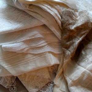 May include: A stack of white and cream lace fabric with intricate patterns. The fabric is soft and delicate, and it would be perfect for crafting or sewing projects.