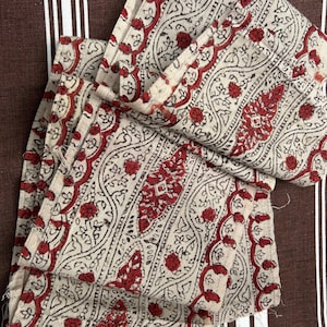 May include: A folded piece of fabric with a red and white paisley pattern. The fabric is folded in a way that shows the pattern on both sides.