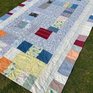 May include: A patchwork quilt featuring a mix of floral and geometric patterns in shades of blue, red, yellow, and white. The quilt is made from various fabrics and textures, resulting in a distinctive and eye-catching design.