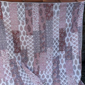 May include: A patchwork quilt with a variety of floral and striped patterns in shades of red, white, and gray. The quilt is rectangular and appears to be handmade, with a white border.