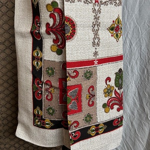 Puede incluir: Una tela blanca con un patrón geométrico colorido. El patrón presenta motivos florales rojos, verdes, amarillos y negros. La tela tiene una superficie texturizada.
