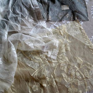 May include: Two layers of white lace fabric with delicate floral patterns. The top layer is sheer and has a more open weave, while the bottom layer is denser and has a more intricate design.