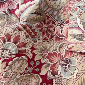 May include: Close-up of a fabric with a repeating floral pattern. The design features large, stylized flowers in shades of red, pink, and beige, set against a deep red background. The fabric has a vintage, ornate aesthetic.