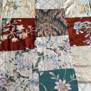 May include: A patchwork quilt with a variety of floral patterns in shades of green, brown, white, and red. The quilt is made of different fabrics and textures, creating a unique and interesting design.