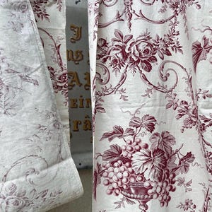 Könnte beinhalten: Weißer Stoff mit einem bordeauxfarbenen Blumen- und Traubenmuster. Der Stoff weist ein sich wiederholendes Muster aus Rosen, Trauben und verzierten Vasen auf. Das Design erinnert an klassische Toile-Muster, geeignet für Heimdekoration oder Bastelprojekte.