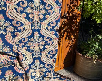 May include: A navy blue fabric with an intricate paisley pattern in cream, peach, and light blue. The fabric is draped, revealing the detailed design and texture. The pattern features floral and swirling elements.