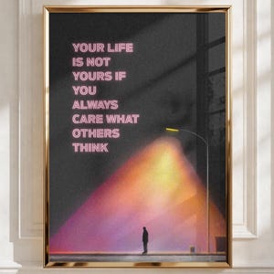 May include: A framed wall art print featuring a dark background with a lone figure standing under a streetlamp. The text in pink neon-style lettering reads: YOUR LIFE IS NOT YOURS IF YOU ALWAYS CARE WHAT OTHERS THINK. The scene has a grainy texture.