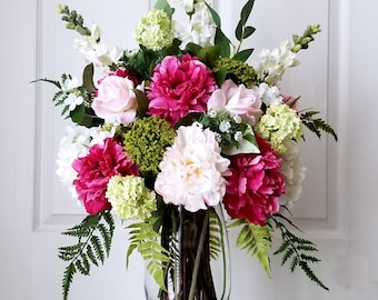 May include: A floral arrangement in a clear glass vase with pink and white peonies, white roses, green foliage, and white snapdragons.