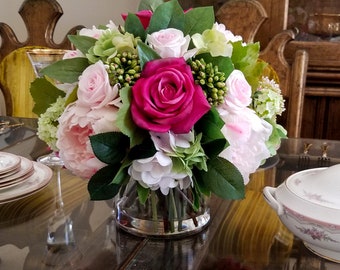 May include: A pink and white flower arrangement in a clear glass vase. The arrangement includes roses, peonies, and hydrangeas.
