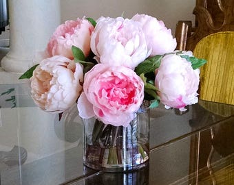 May include: A bouquet of pink and white peonies arranged in a clear glass vase. The flowers are in full bloom and have a delicate, feminine appearance.