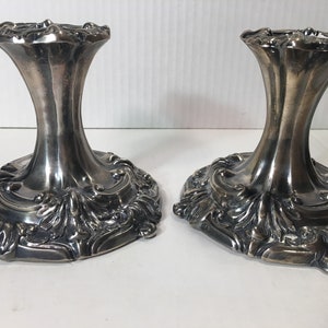 May include: A pair of silver candle holders with ornate, detailed designs. The holders have a wide base and a tall, slender stem.