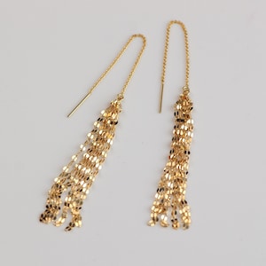 May include: A pair of gold dangle earrings with a long, thin chain tassel. The earrings are made of multiple strands of chain that are connected together.