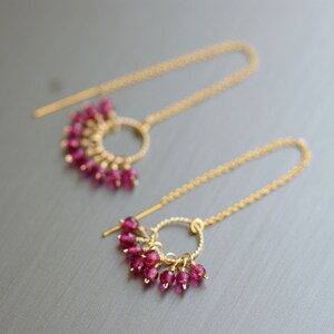 Pode incluir: Um par de brincos de ouro com um design circular e contas cor-de-rosa penduradas.