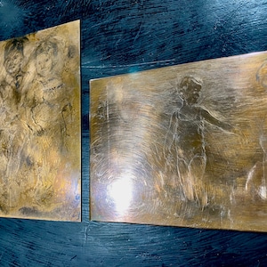 Peut inclure: Deux plaques rectangulaires en laiton avec des images gravées de personnes. Les plaques ont une teinte dorée chaude et une surface légèrement texturée.