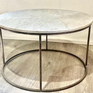 May include: A round coffee table with a white marble top and a dark metal frame. The table has a circular base and four legs that connect to the tabletop. The table is approximately 30 inches in diameter.