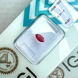 Peut inclure: Un rubis rouge taille marquise pesant 0,31 ct, fixé dans un boîtier de présentation en plastique transparent. Le boîtier porte les inscriptions 1805667602, 0,31 Ct et RUBY, ainsi que le logo et le texte de l'International Gemological Institute.