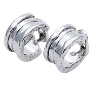 May include: A pair of silver-toned metal hoop earrings featuring a multi-layered, coiled design with the text BVLGARI engraved along the outer edges. The earrings have a polished, reflective finish and a thick, rounded structure with a hollow center.