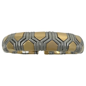 May include: A gold and silver-toned bracelet with a geometric design. The bracelet features alternating gold and silver-colored hexagonal segments, creating a flexible, articulated band. The design is modern and elegant.