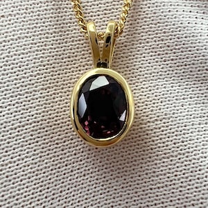 May include: A gold pendant necklace with a dark purple oval gemstone.
