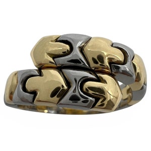 May include: A two-tone gold and silver ring with a puzzle-like design. The ring is made of interlocking pieces that form a continuous pattern.