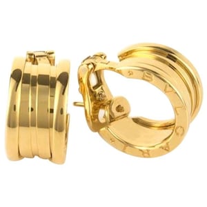 May include: A pair of gold hoop earrings featuring a multi-band design with a smooth, polished finish. The side of the hoop is engraved with the text BVLGARI. These earrings have a hinged clip-on mechanism for secure attachment to the earlobe.