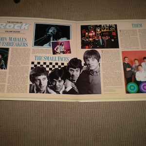 May include: A double-page spread from a book titled "The History of Rock, Volume Eleven." The left page features a black and white photo of John Mayall's Bluesbreakers, and the right page features a black and white photo of The Small Faces and a color photo of Them.