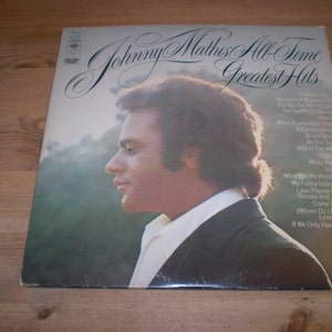 May include: A vinyl record cover featuring a portrait of Johnny Mathis, a singer, with the title "Johnny Mathis All-Time Greatest Hits" and a list of songs on the back.