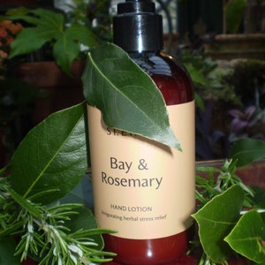 May include: A brown glass bottle of Bay & Rosemary hand lotion with a black pump top. The bottle is surrounded by green leaves. The label reads "Bay & Rosemary Hand Lotion Invigorating herbal stress relief."